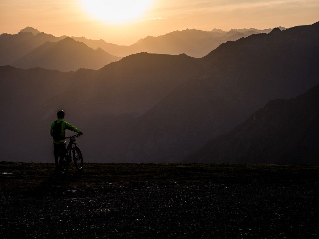 Cycliste sur une crête devant des montagnes au coucher du soleil
